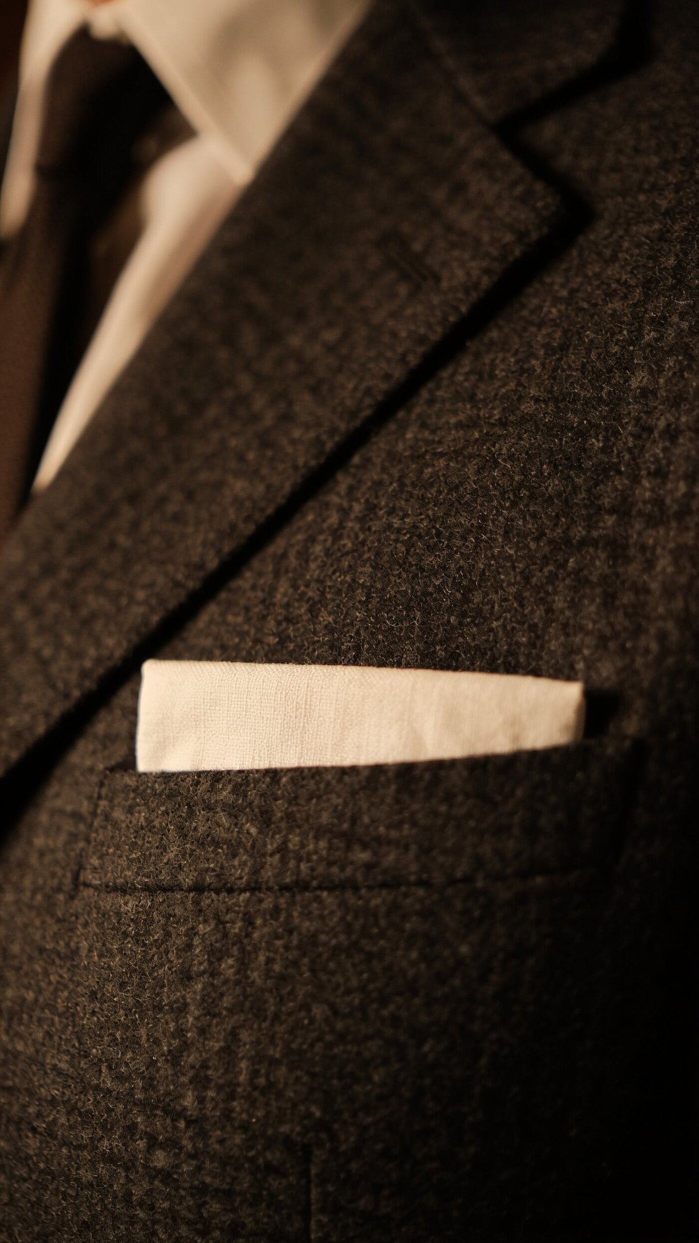 A white linen pocket square in a flat fold sitting just above the breast pocket