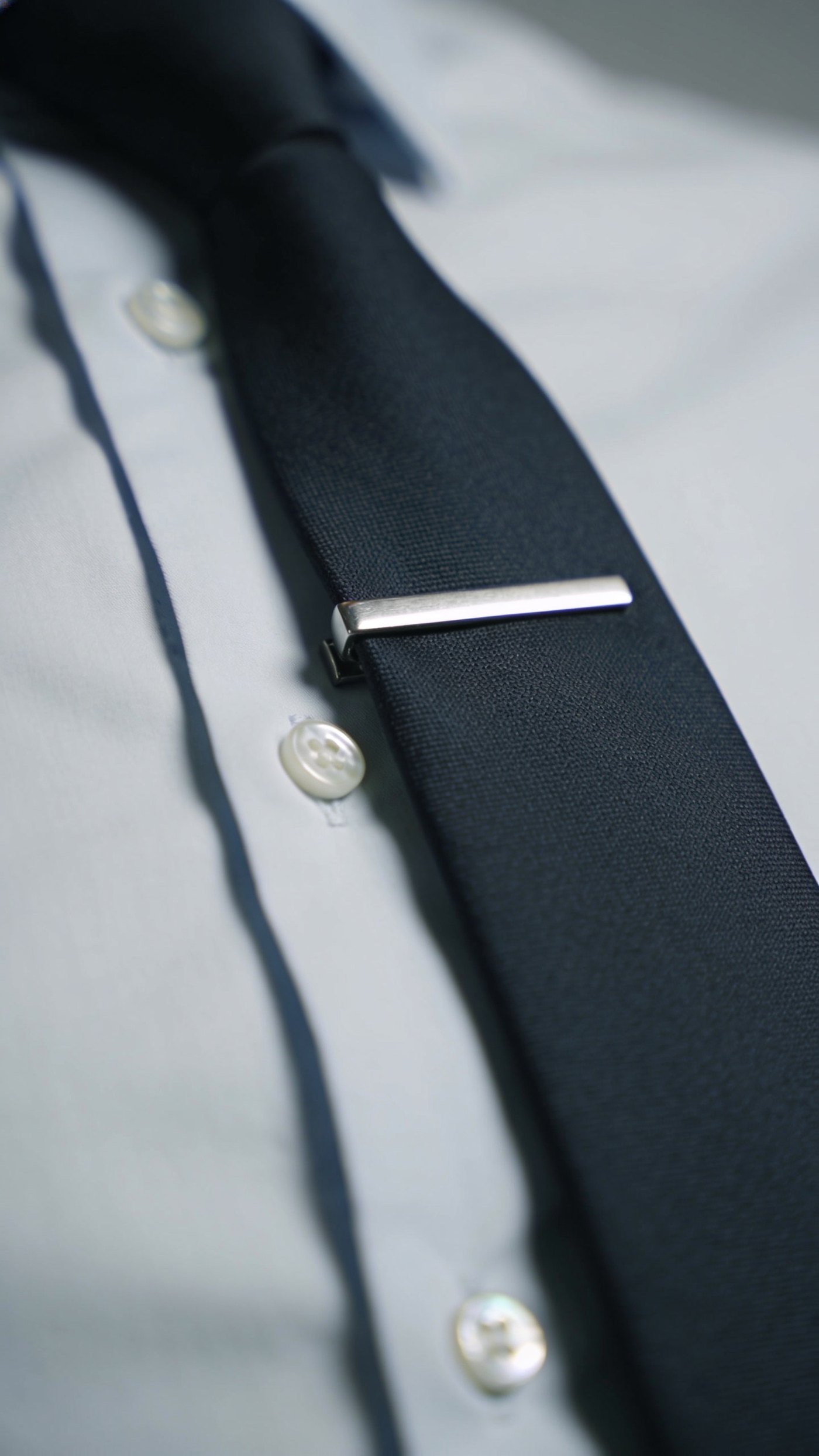 A narrow silver tie bar holding a slim tie flat against the shirt