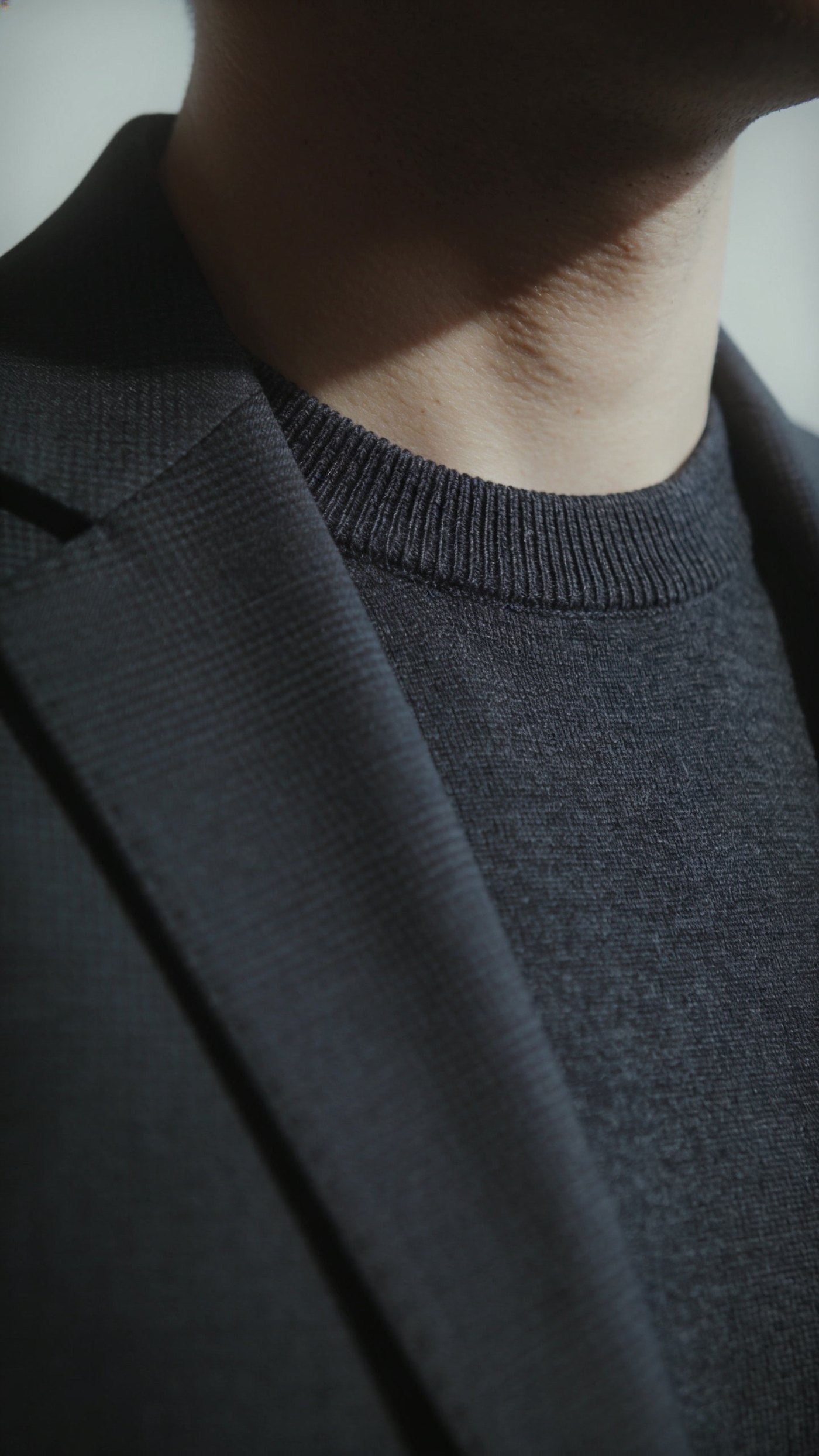 A fine gauge dark crew neck worn under a suit jacket with no shirt collar
