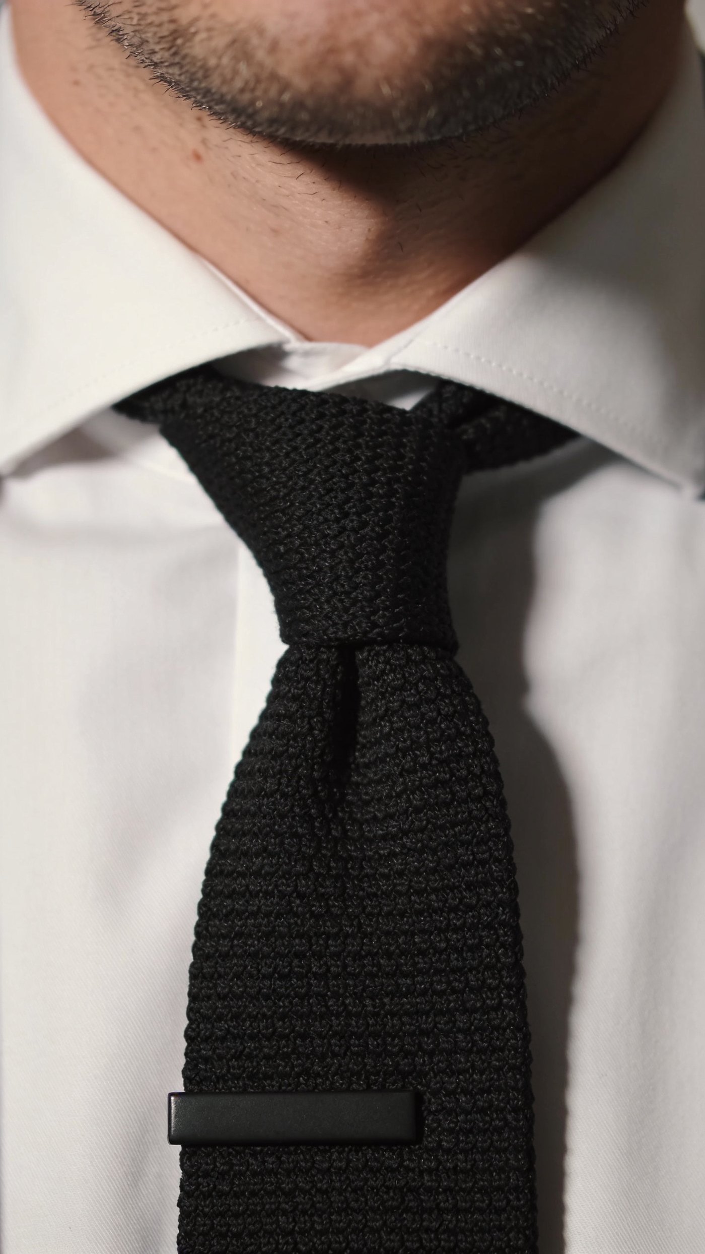 A matte knitted tie with a square flat end against a dark suit
