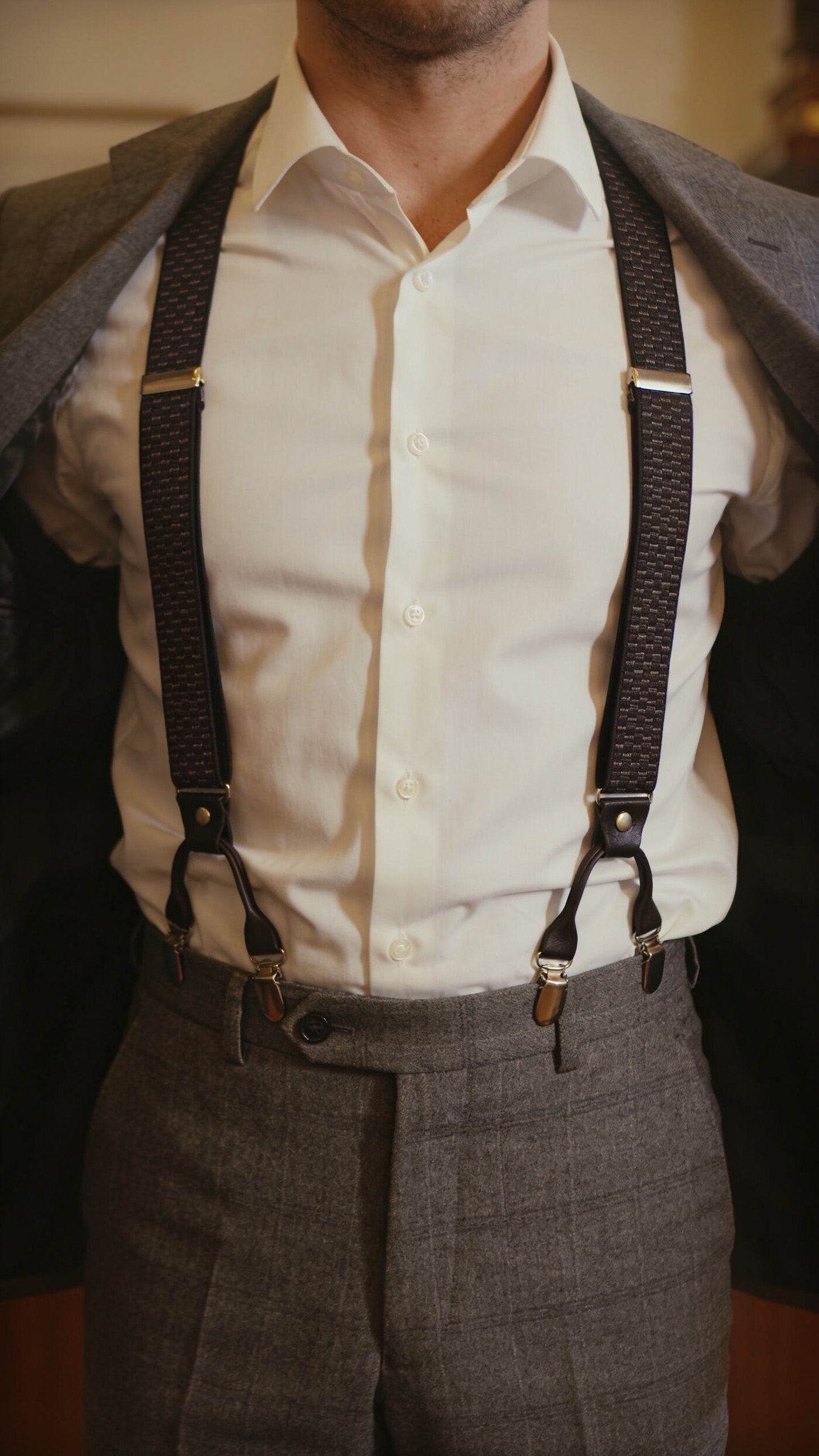 Woven braces over a shirt holding a high rise trouser from the shoulder