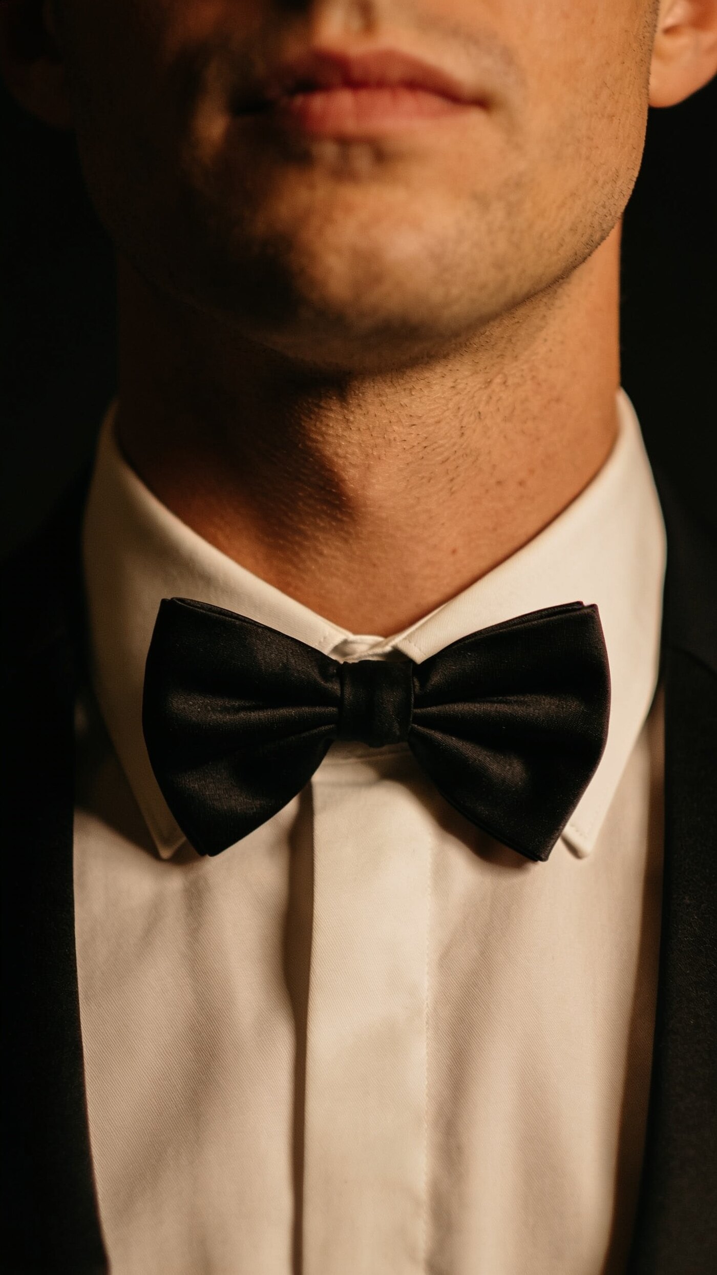 A hand tied black silk bow tie closing the collar of a formal shirt